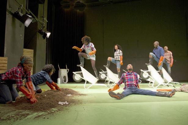 Eine Theaterszene mit mehreren Darstellern, die mit Schubkarren und Erde interagieren.