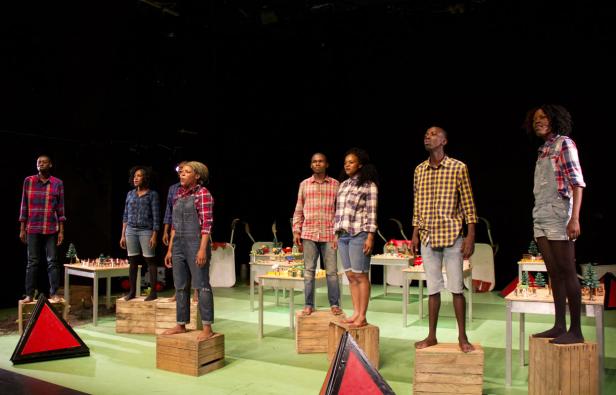 Eine Gruppe von Schauspieler:innen steht barfuß auf Holzkisten auf einer Bühne.
