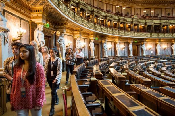 Eine Gruppe von Menschen besichtigt einen reich verzierten Saal mit Statuen und Sitzreihen.
