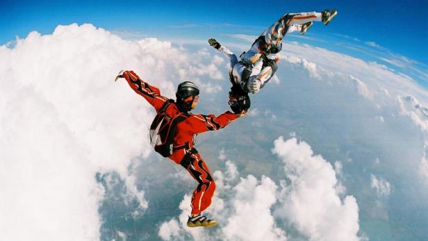 Eine Archivaufnahme von Fabian Raidel beim Fallschirmspringen. Zwei Fallschirmspringer führen einen Stunt hoch über den Wolken aus.