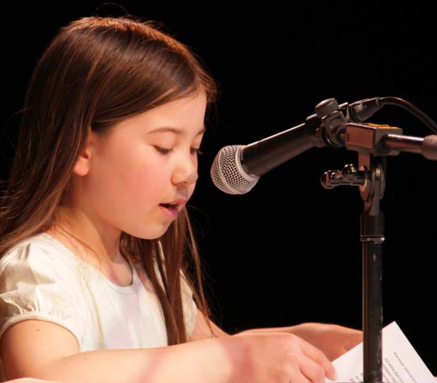 Ein junges Mädchen liest am Mikrofon einen Text von Alisa Strasser vor.