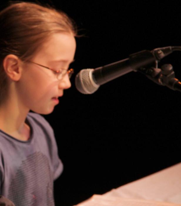 Ein junges Mädchen mit Brille liest vor einem Mikrofon.