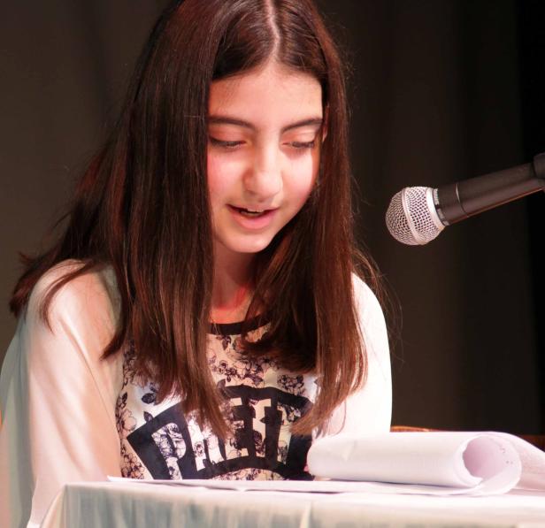 Ein junges Mädchen liest vor einem Mikrofon von einem Blatt Papier ab.