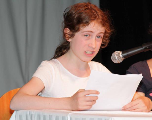 Ein junges Mädchen liest mit einem Mikrofon vor Publikum von einem Blatt Papier ab.