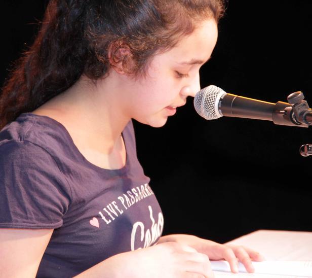 Eine junge Frau liest am Mikrofon von einem Blatt Papier ab.