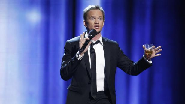 Neil Patrick Harris moderierte den Abend. Neil Patrick Harris hält ein Glas Whiskey und ein Mikrofon auf einer Bühne.