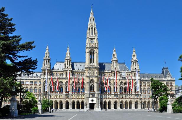 Das Wiener Rathaus mit rot-weißen Flaggen geschmückt vor blauem Himmel.