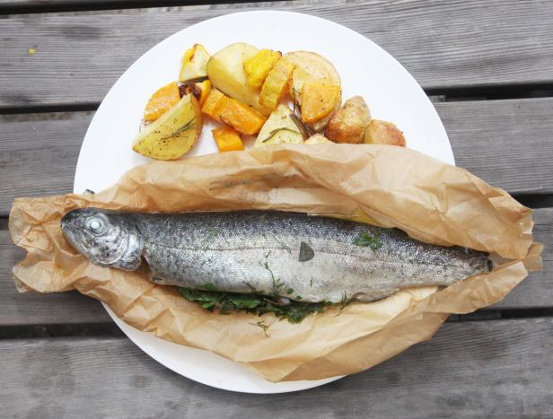 Ein ganzer Fisch in Backpapier mit geröstetem Gemüse auf einem Teller.