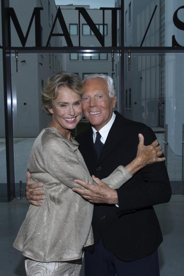 Giorgio Armani umarmt eine Frau vor einem Gebäude mit der Aufschrift „MANI“.