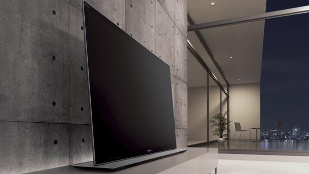 Ein moderner Fernseher steht vor einer Betonwand in einem minimalistischen Wohnzimmer mit Blick auf eine Stadt bei Nacht.