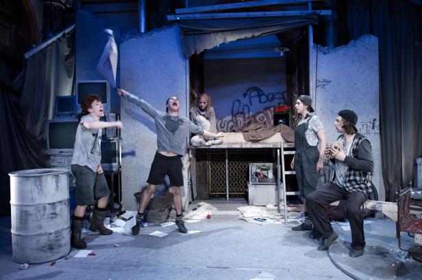 Eine Theaterszene mit einer Gruppe junger Schauspieler in einer urbanen Ruinenkulisse.