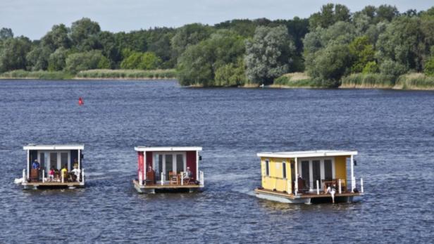 Drei bunte Hausboote fahren auf einem See.