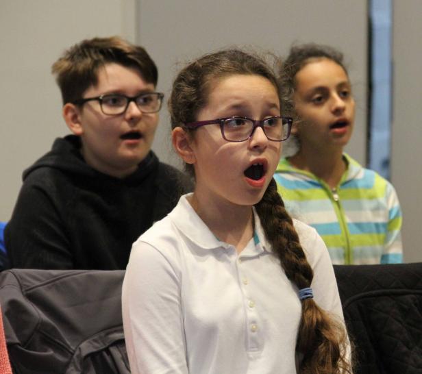 Drei Kinder mit offenem Mund, möglicherweise bei einem Chorauftritt.