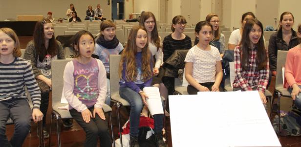 Eine Gruppe von Kindern sitzt in einem Raum und singt gemeinsam.