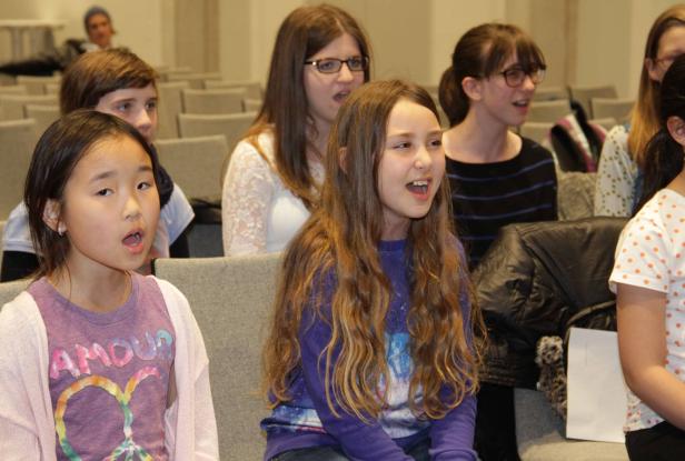 Eine Gruppe junger Menschen sitzt und singt in einem Raum.