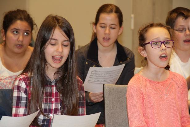 Eine Gruppe von Kindern singt gemeinsam aus Notenblättern.