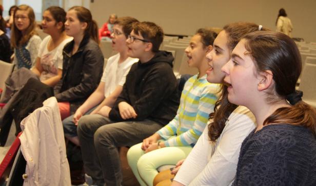 Eine Gruppe von Jugendlichen sitzt und singt in einem Raum.