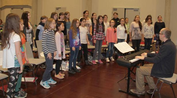 Ein Kinderchor probt mit einem Mann am Keyboard.