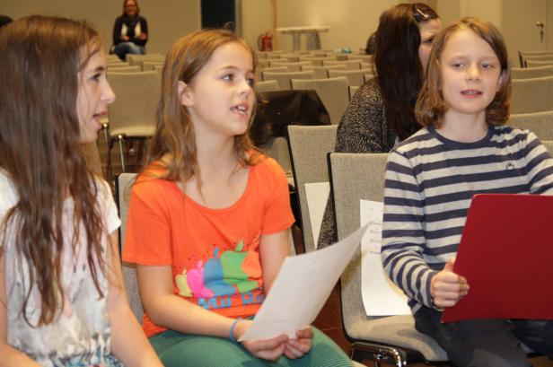 Drei Kinder sitzen in einem Raum und halten Notenblätter in der Hand.