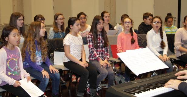 Eine Gruppe von Kindern sitzt und singt in einem Chor, begleitet von einem Klavier.