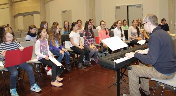 Ein Jugendchor singt unter der Leitung eines Mannes, der Klavier spielt.