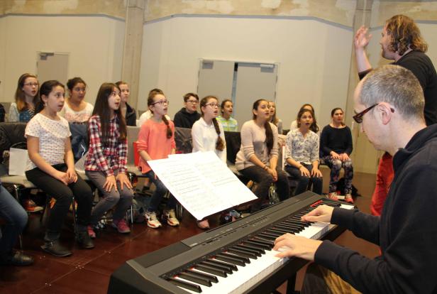 Ein Chor von Jugendlichen singt unter der Leitung eines Dirigenten und eines Pianisten.