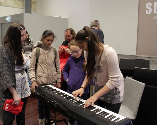 Eine junge Frau spielt auf einem Keyboard, umgeben von mehreren Kindern.