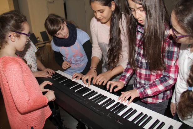 Mehrere junge Mädchen spielen gemeinsam auf einem elektronischen Klavier.