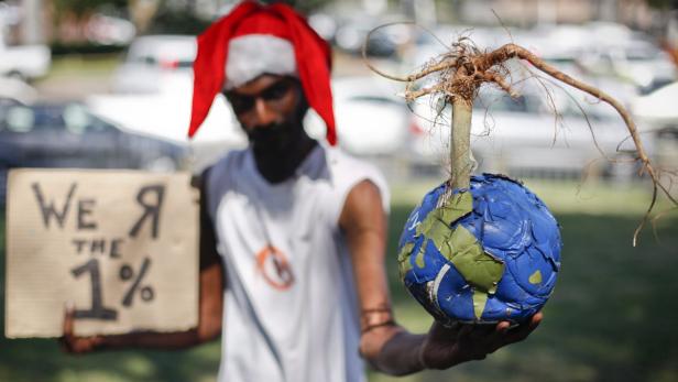 Durban, Weltklimagipfel, Umweltschutz Ein Mann mit Weihnachtsmütze hält ein Schild mit der Aufschrift „We are the 1%“ und eine Weltkugel mit einem Baum darauf.
