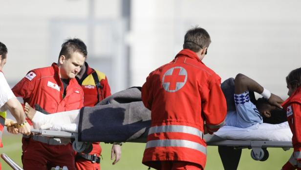 Sanitäter schieben einen verletzten Fußballspieler mit einem gebrochenen Bein auf einer Trage.