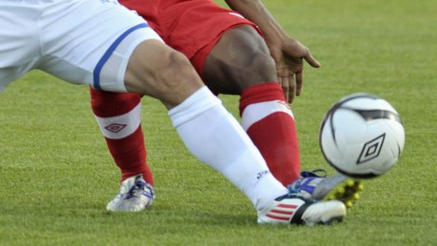 Zwei Fußballspieler kämpfen um den Ball auf einem grünen Rasen.