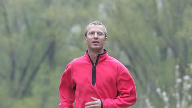 Ein Mann mit Brille und rotem Pullover joggt im Freien.