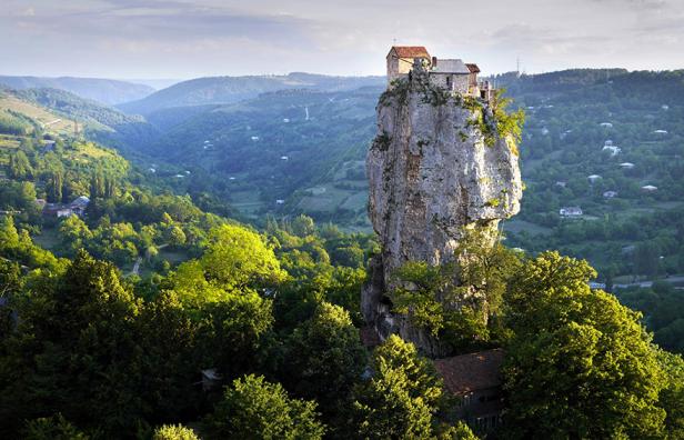 Ein Kloster steht auf einem hohen Felsen inmitten einer grünen Landschaft.