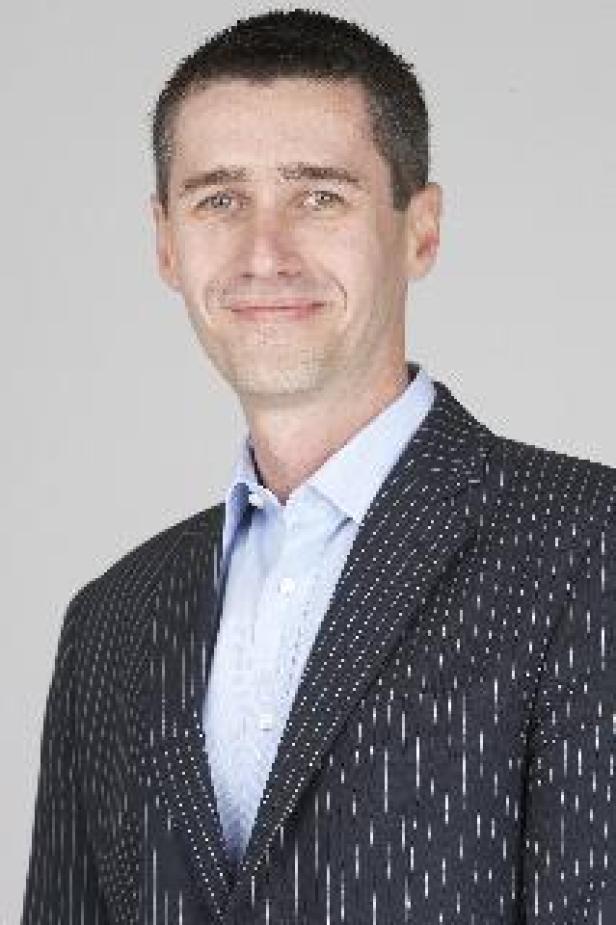Ein Mann mit dunklen Haaren und einem gestreiften Sakko lächelt in die Kamera.