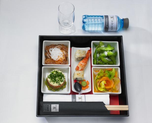 Ein Bento-Box mit Sushi, Edamame, Salat und anderen Speisen, zusammen mit einer Wasserflasche.