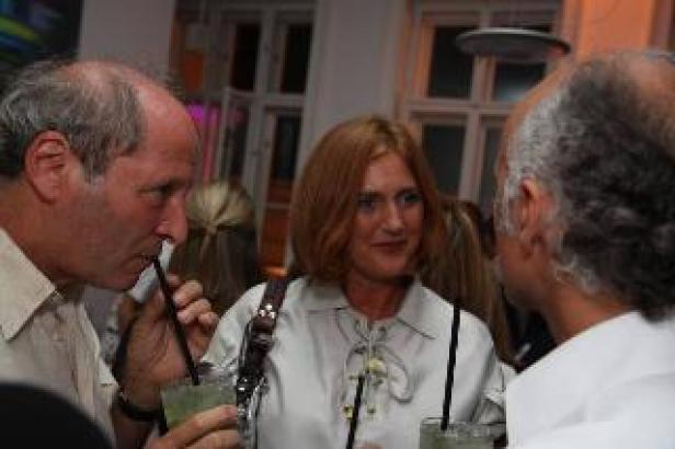 Drei Personen unterhalten sich auf einer Party, zwei trinken Cocktails.
