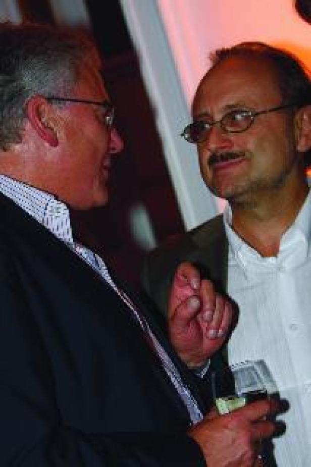 Zwei Männer unterhalten sich, einer hält ein Glas Weißwein.
