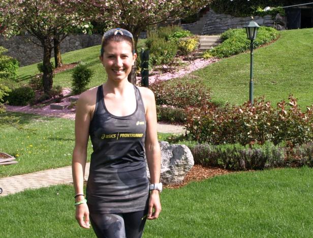 Eine Frau im Sportoutfit steht in einem Garten.