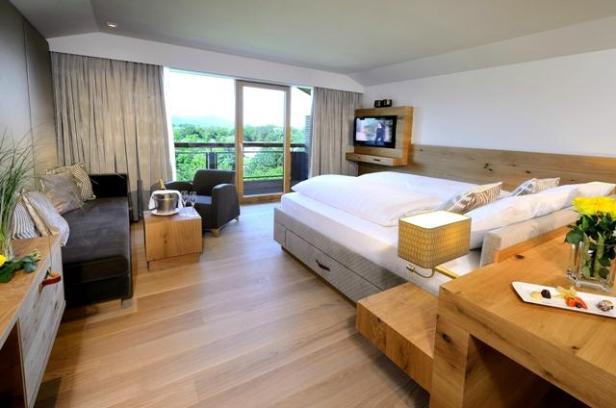 Ein helles Hotelzimmer mit Doppelbett, Sitzecke und Balkon mit Blick ins Grüne.