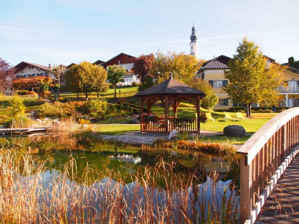 Ein malerischer Blick auf einen See mit einem Pavillon und Wohnhäusern im Hintergrund.