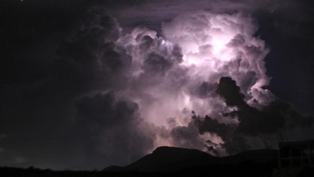 Ein Gewitter mit Blitzen erhellt den Nachthimmel über einer dunklen Landschaft.
