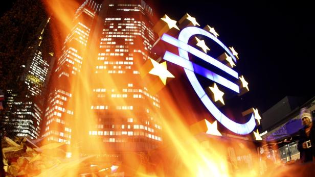 Das Euro-Symbol leuchtet vor einem Hochhaus bei Nacht.