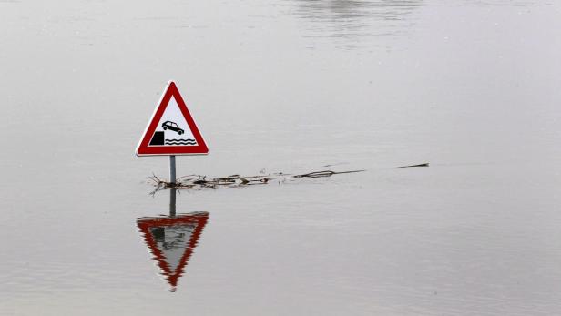 Ein Warnschild vor einer überfluteten Straße steht im Wasser.