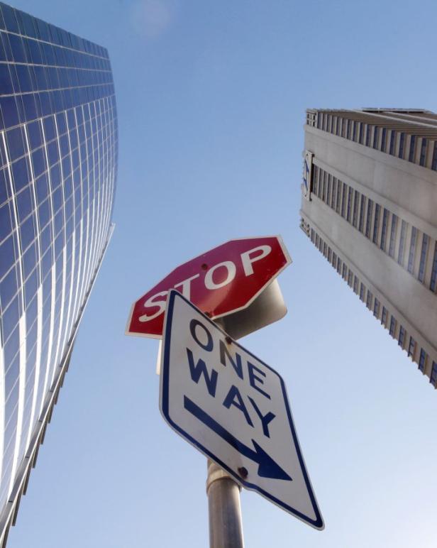 Ein Stoppschild und ein Einbahnstraßenschild vor dem Hintergrund von zwei Hochhäusern.