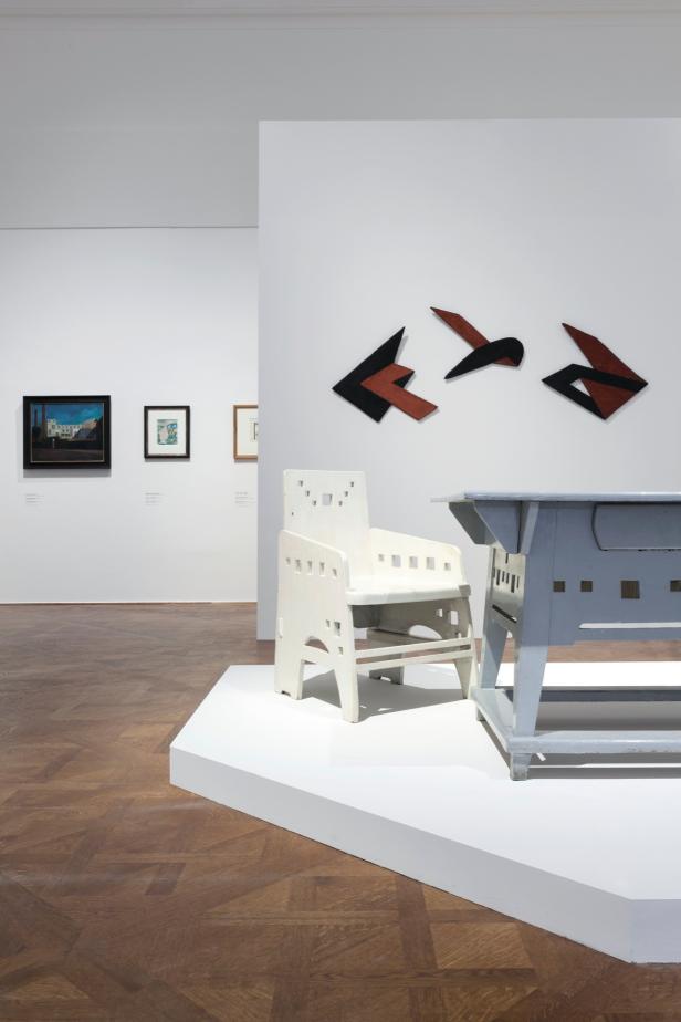 Ein weißer Stuhl und ein grauer Tisch stehen in einem Ausstellungsraum.