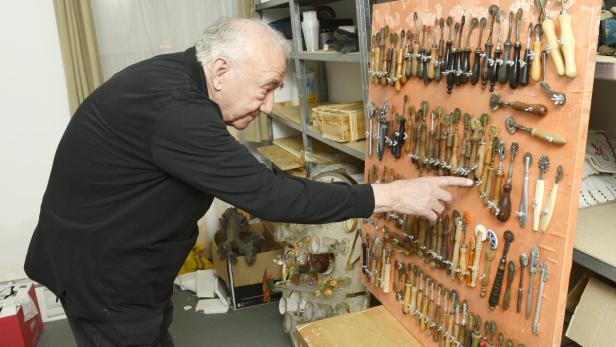 Ein älterer Mann betrachtet eine Sammlung von Rollschneidern an einer Wand.