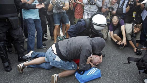 Ein Polizist fixiert einen Demonstranten am Boden, umringt von anderen Polizisten und Fotografen.