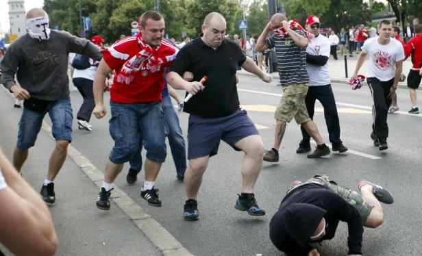 Eine Gruppe von Fußballfans läuft auf einer Straße, einige tragen polnische Farben.