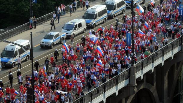 Eine Menschenmenge mit russischen Flaggen marschiert über eine Brücke, begleitet von Polizeifahrzeugen.