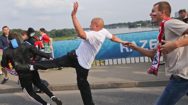 Ein Mann tritt einen anderen Mann, während ein Dritter mit polnischer Flagge im Gesicht daneben steht.